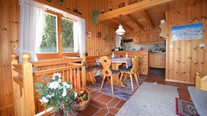 A wooden cabin interior with a dining area, kitchen, and a large window. - Chalet Joshua (Heremence)