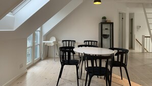 Tilava huone, jossa on korkea katto, kattovalokuvio ja pyöreä ruokapöytä mustilla tuoleilla.