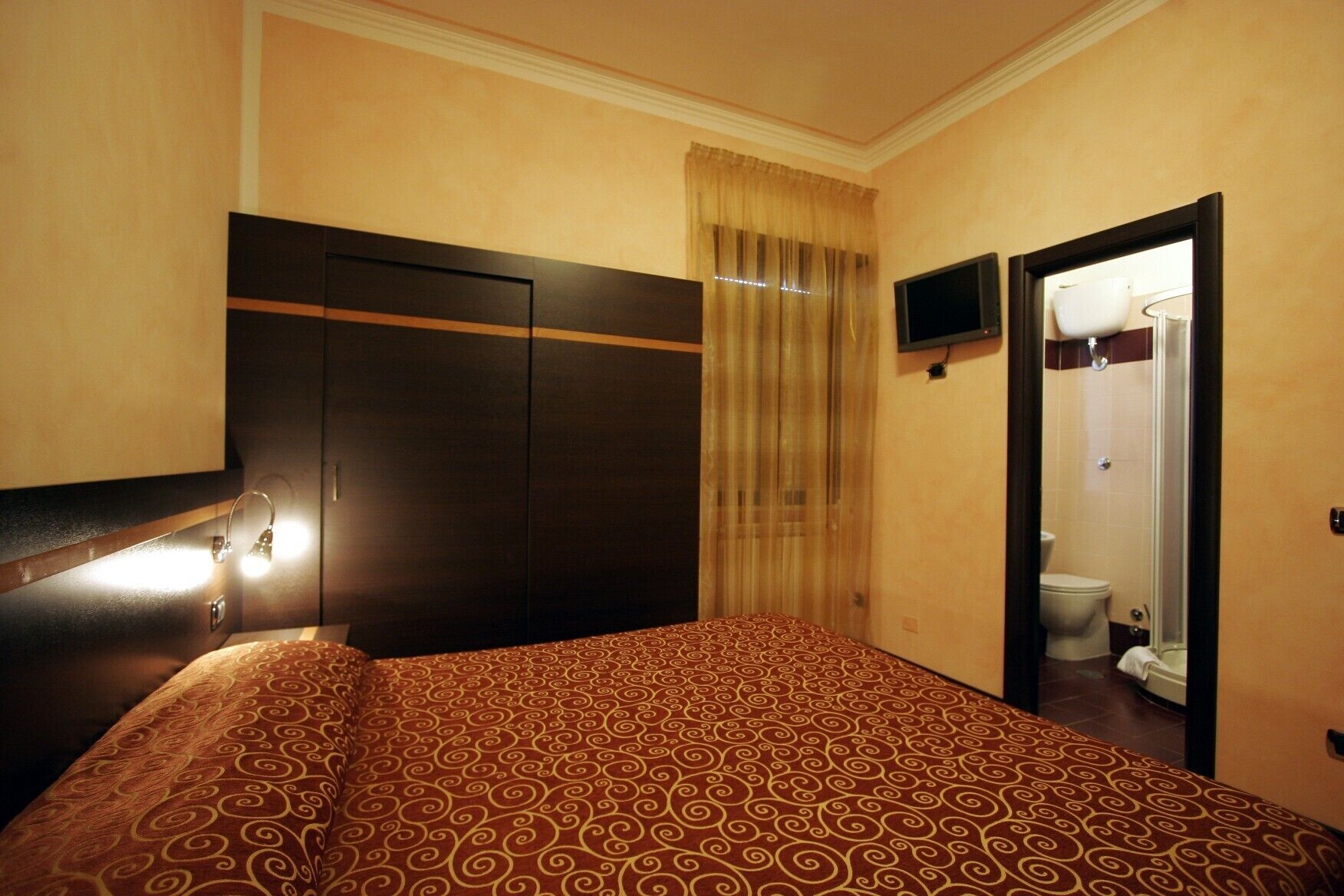 A hotel room with a bed, a TV mounted on the wall, and a bathroom visible through an open door.