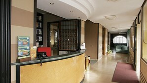Un espace d’accueil d’hôtel avec un comptoir d’accueil incurvé, une chaise rouge, un téléphone et un panneau d’affichage sur lequel est inscrit un message de bienvenue.
