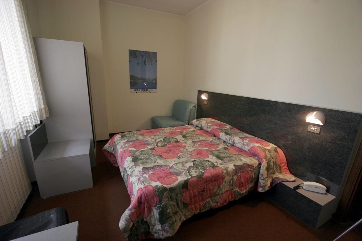 A bedroom with a bed, a nightstand, a chair, a poster on the wall, and a window with curtains.