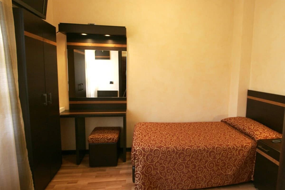 Una habitación de hotel compacta con una cama individual, un pequeño escritorio con espejo y un armario.