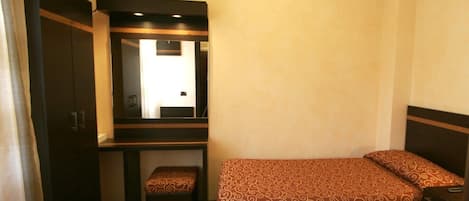 Una habitación de hotel compacta con una cama individual, un pequeño escritorio con espejo y un armario.