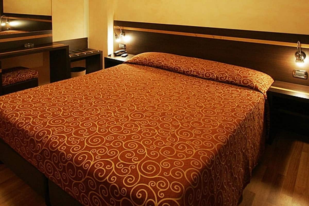 Habitación de hotel con una cama grande, un escritorio con silla, televisor y una mesita de noche con lámpara.