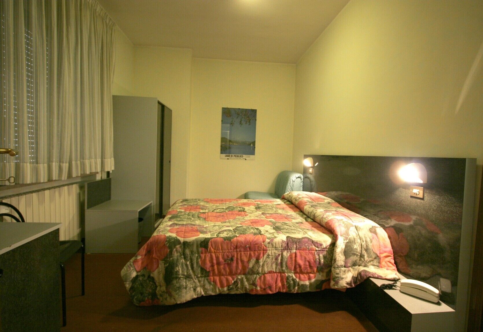 Un dormitorio con una cama, un escritorio, una silla, una mesita de noche, una lámpara y un cartel en la pared.