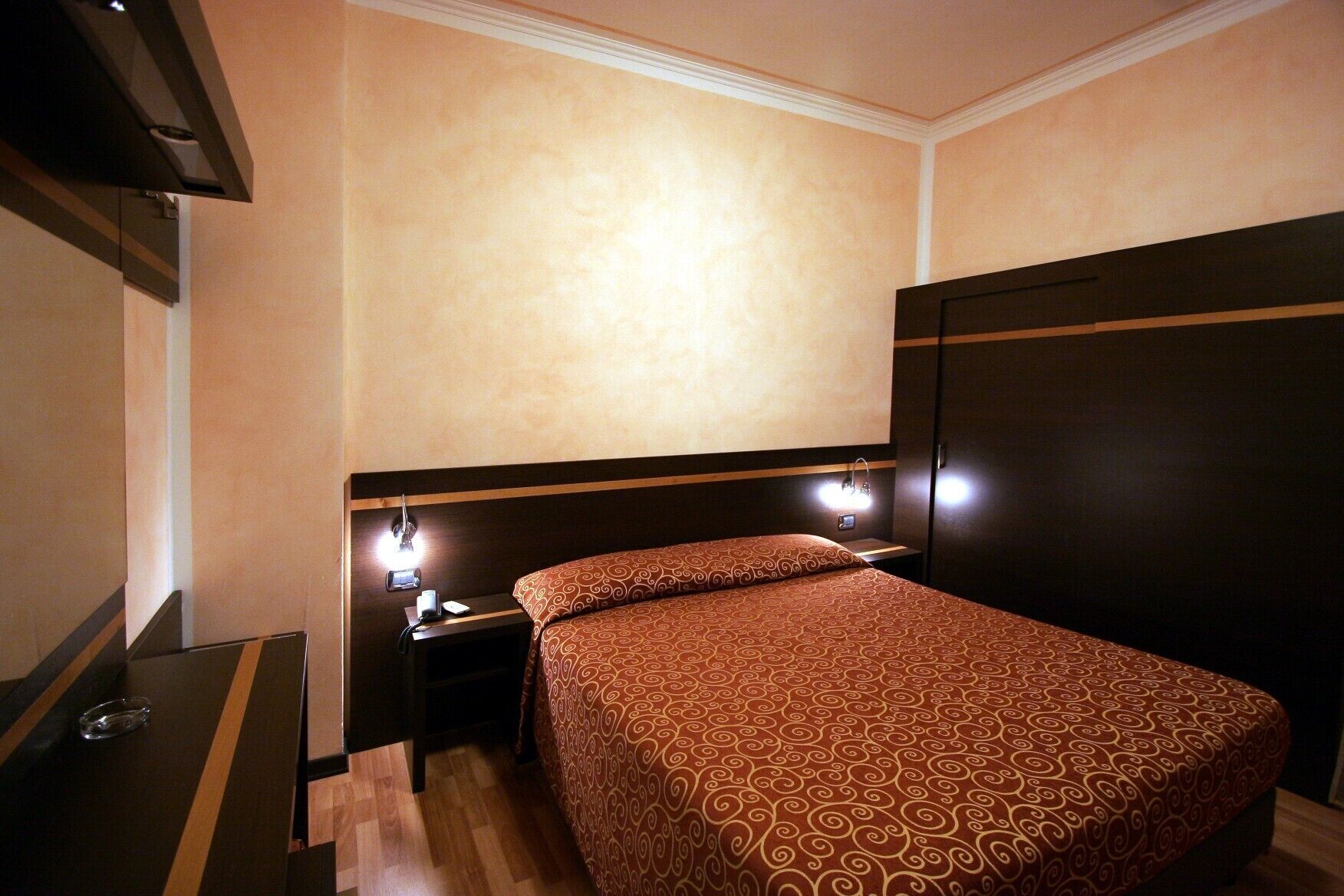 A hotel room with a bed, a nightstand, a mirror, and a wardrobe.