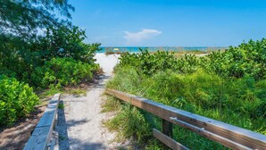 A sandy beach path with a wooden railing, surrounded by greenery and leading to a beach. - Beach Bliss: Perfect location, pool, views, steps to beach (Anna Maria)