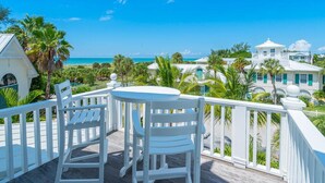 A wooden deck with two white chairs, overlooking a beach with palm trees and a clear blue sky. - Beach Bliss: Perfect location, pool, views, steps to beach (Anna Maria)