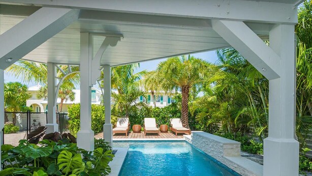 A pool area with white pillars, lounge chairs, and tropical plants. - Beach Bliss: Perfect location, pool, views, steps to beach (Anna Maria)