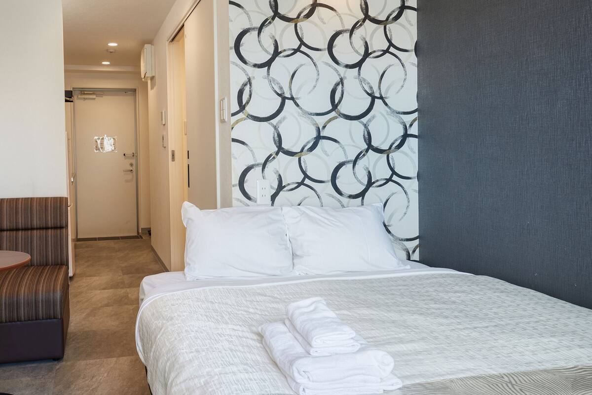 A hotel room with a bed, a small round table, a chair, and a patterned wall.