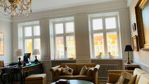 A spacious living room with a large window, a chandelier, and a comfortable seating area. - Best Stay Copenhagen - Nyhavn 8 (Copenhagen)
