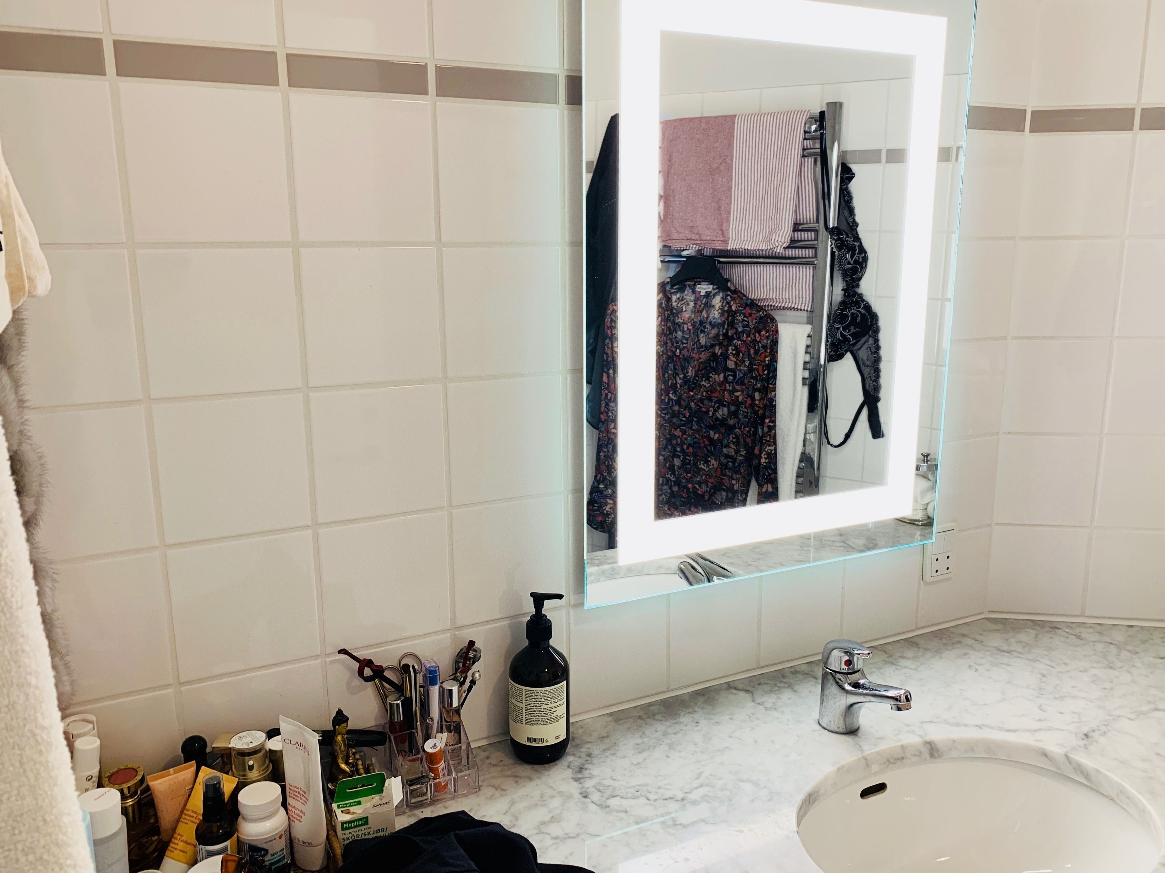 A bathroom with a large mirror, a sink, and toiletries on the counter.