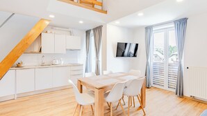 A modern kitchen with white cabinets, a wooden dining table with chairs, and a TV mounted on the wall. - Apartmaji Skok (Bovec)