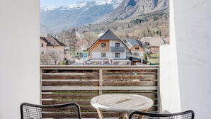 A balcony with a wooden table and chairs, overlooking a town with houses and mountains in the background. - Apartmaji Skok (Bovec)