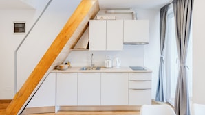 A modern kitchen with white cabinets, a wooden staircase, a sink, and a kettle. - Apartmaji Skok (Bovec)