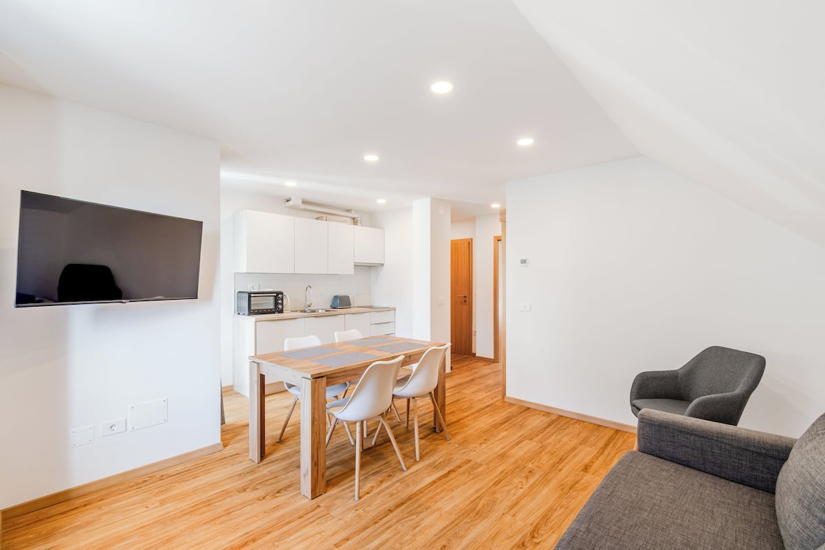 A modern apartment with a dining area, kitchenette, and a gray sofa.