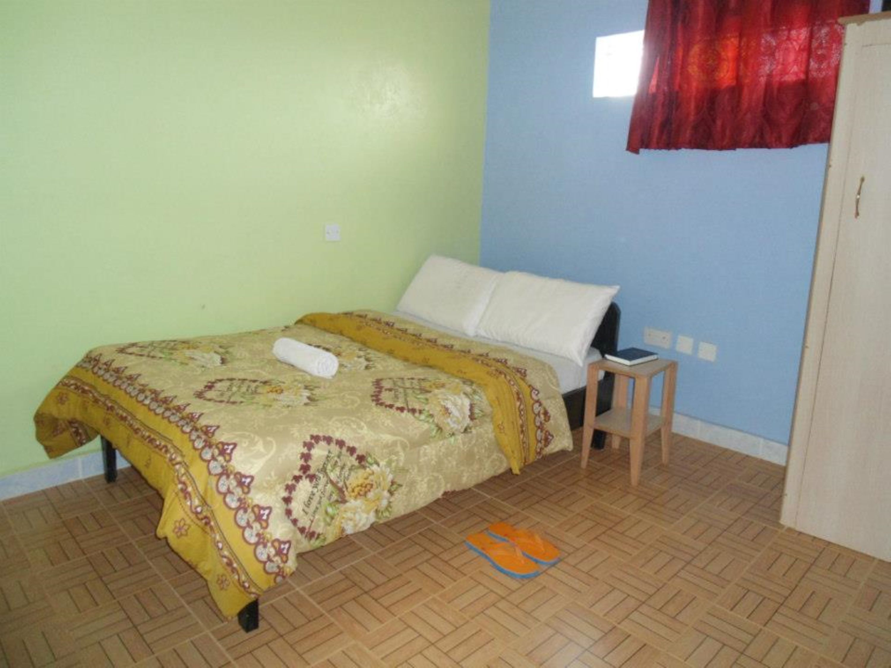 A room with a bed, a small wooden stool, and a pair of flip-flops on the floor.