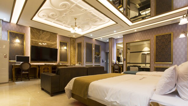 A hotel room with a large bed, a desk with a chair, a television, and a bathroom with a mirror. - MYEONPUM DRIVE IN HOTEL (Jeongeup)
