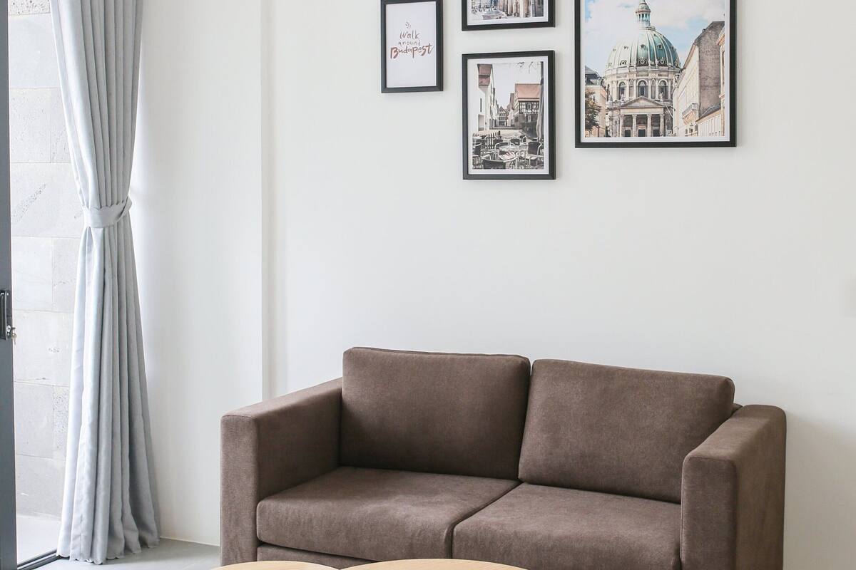 A modern living room with a brown sofa, two wooden side tables, and framed cityscape pictures on the wall.