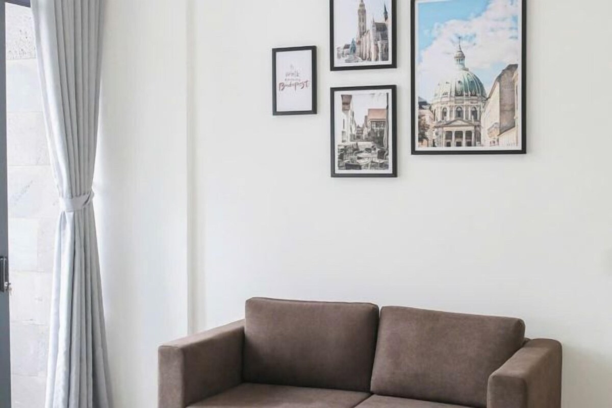A room with a brown sofa, a white wall, and three framed pictures depicting cityscapes.