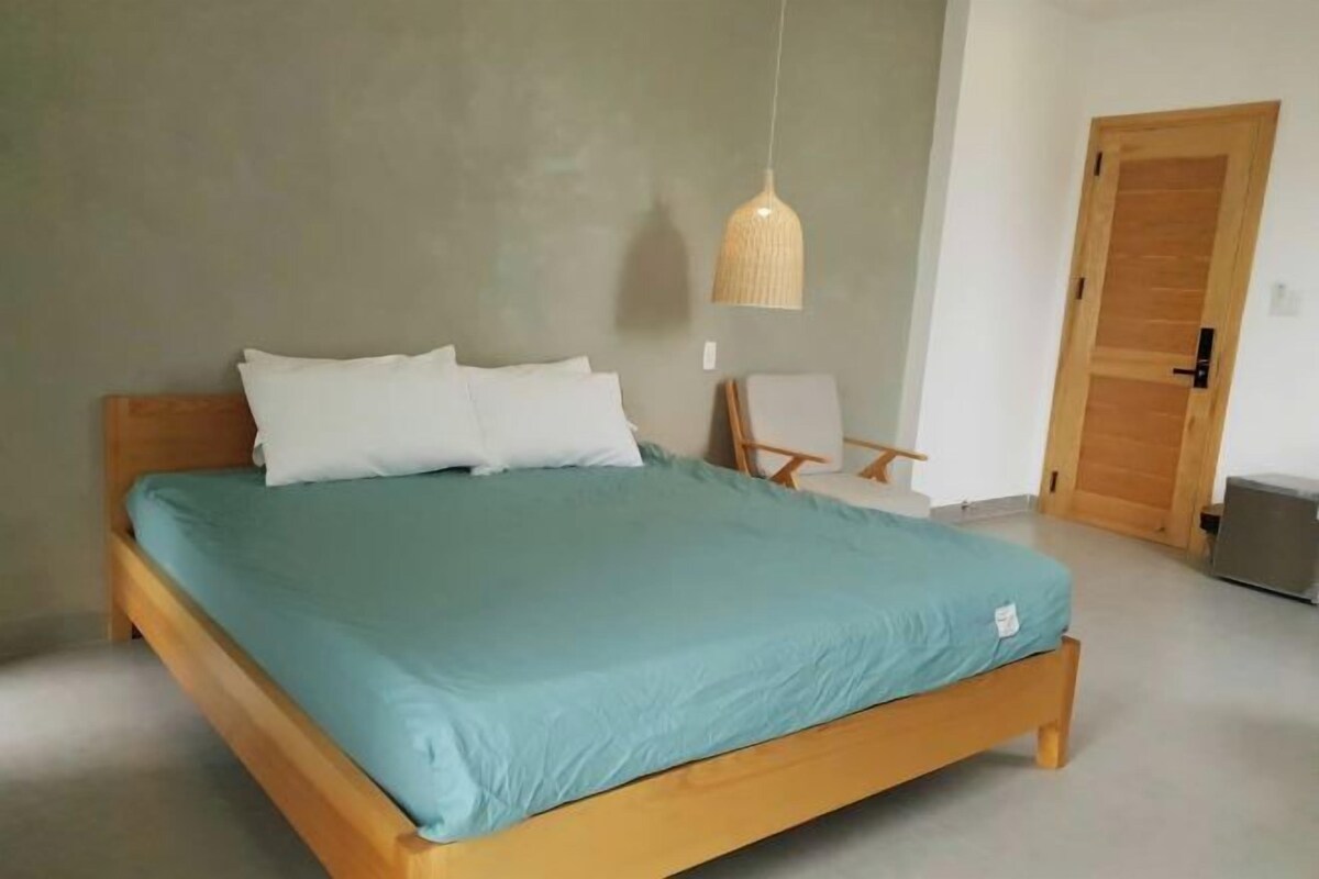 A single-bed room with a wooden frame, teal bedding, and a hanging light fixture.