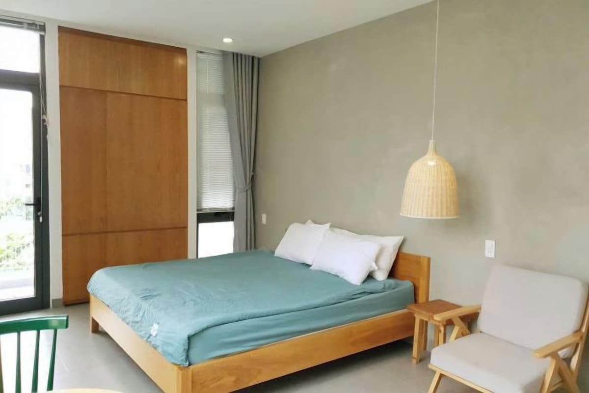 A bedroom with a wooden bed, a green bedspread, a white pillow, a wooden nightstand, a hanging lamp, and a green chair.