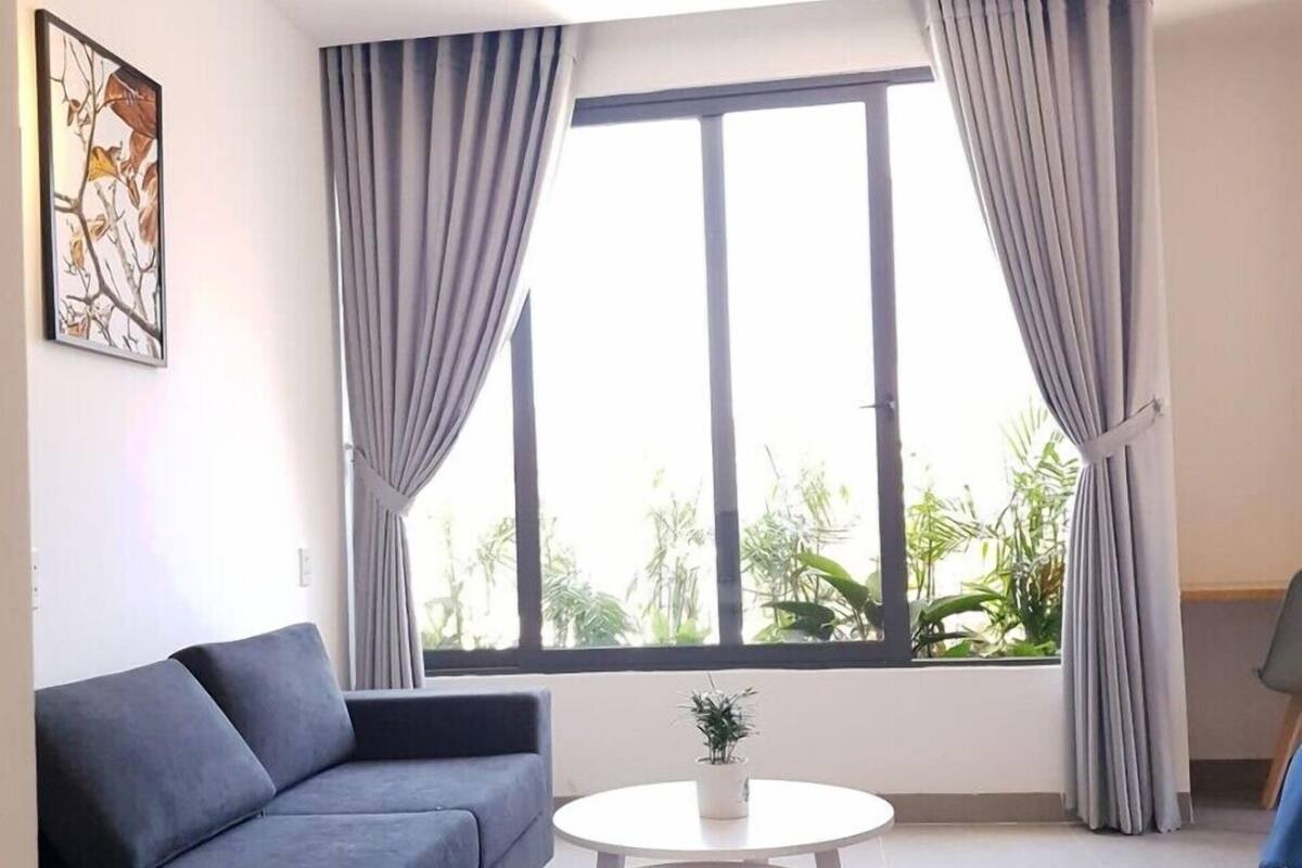 A modern living room with a grey sofa, a round white coffee table, and a large window with grey curtains.