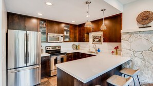 Une cuisine moderne dotée d’appareils électroménagers en acier inoxydable, de meubles de rangement en bois foncé, d’un grand îlot central avec des tabourets, et d’un mur décoratif en pierre.
