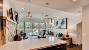Une cuisine moderne dotée d’un grand îlot central, d’un mur d’accent en pierre et offrant une vue sur un jardin avec un barbecue et un espace salon extérieur.