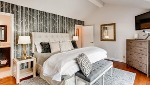 Une chambre à coucher avec un grand lit, un banc, une commode, un téléviseur et un ventilateur de plafond.