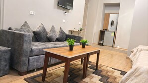 A modern living room with a grey sofa, a wooden coffee table, and a flat-screen TV mounted on the wall. - Holy Sheet Hostel (Cairo)