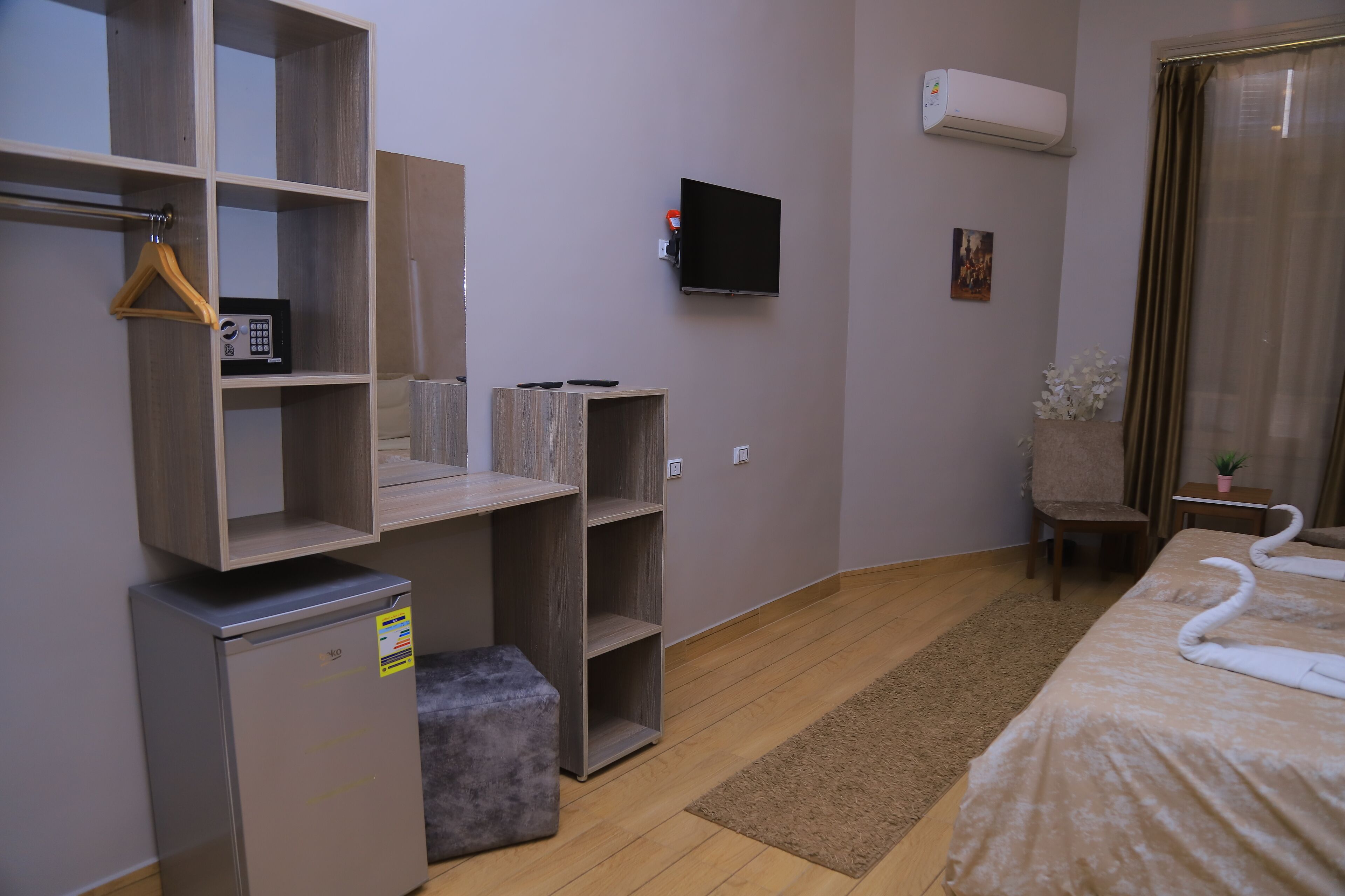 A hotel room with a bed, a TV, a mini-fridge, a wardrobe, and a small table with a plant.