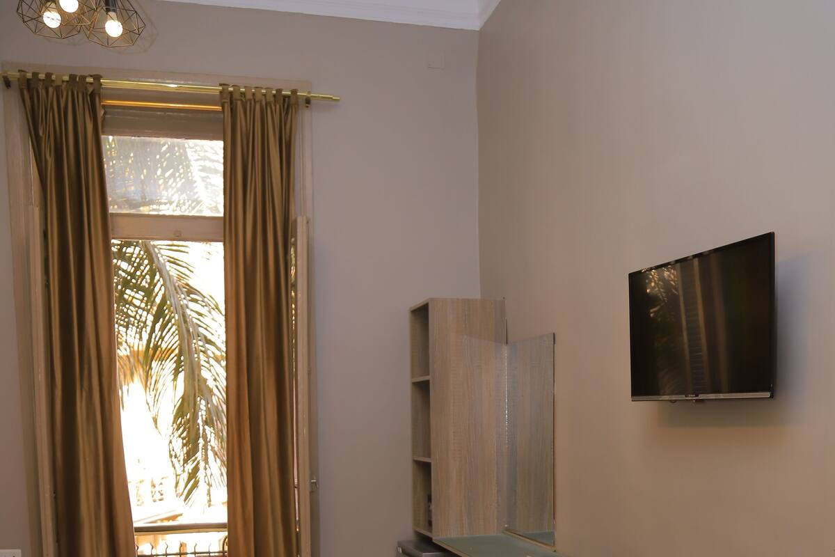 A hotel room with a bed, a desk with a chair, a television, and a view of palm trees outside.