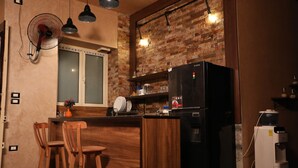 A kitchen with a brick wall, a refrigerator, a water dispenser, and wooden bar stools. - Holy Sheet Hostel (Cairo)