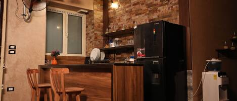 A kitchen with a brick wall, a refrigerator, a water dispenser, and wooden bar stools.