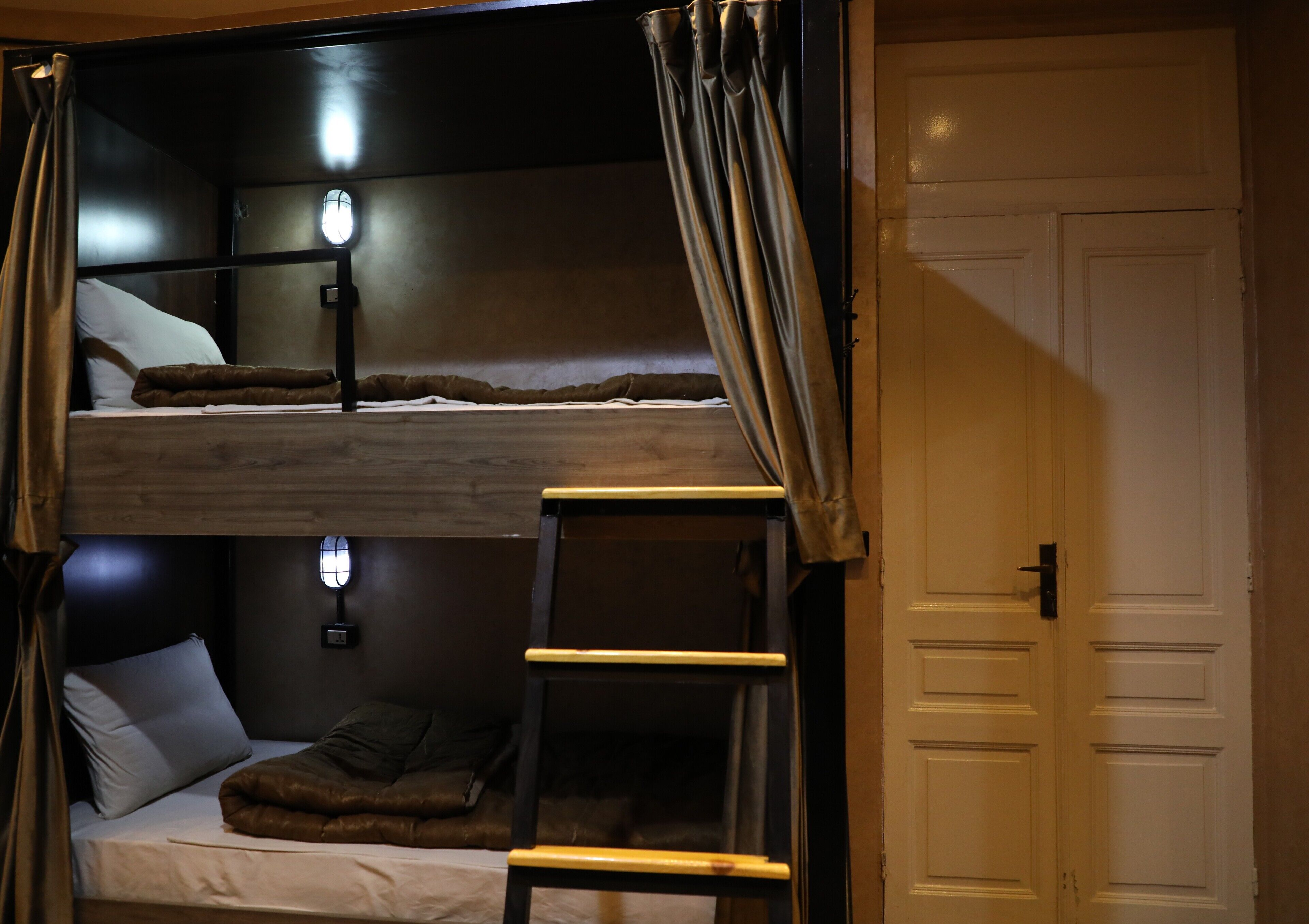 A bunk bed room with a ladder, a bedside table, and a door.