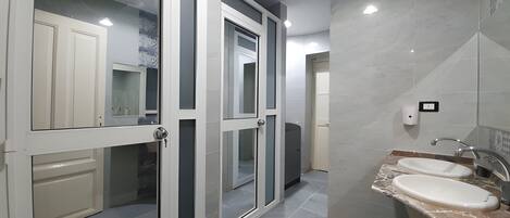 Un baño moderno con entrada de puerta de vidrio, un lavabo con encimera de mármol y zona de ducha.