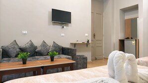 A modern living room with a sofa, a coffee table, a flat-screen TV mounted on the wall, and a small kitchen area with a refrigerator. - Holy Sheet Hostel (Cairo)