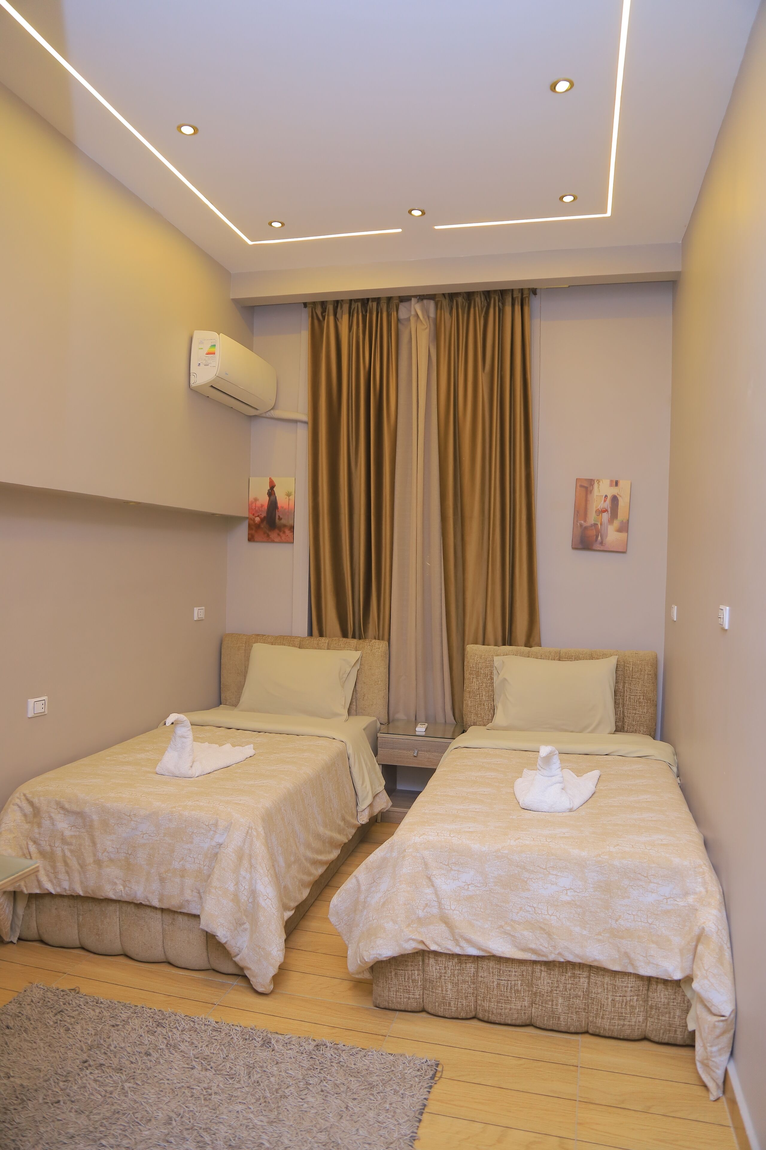 A hotel room with two single beds, beige bedding, a gray rug, and a ceiling with recessed lighting.