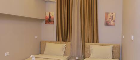 A hotel room with two single beds, beige bedding, a gray rug, and a ceiling with recessed lighting.