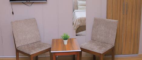 A hotel room with two chairs, a small table with a plant, a TV mounted on the wall, and a large wardrobe.