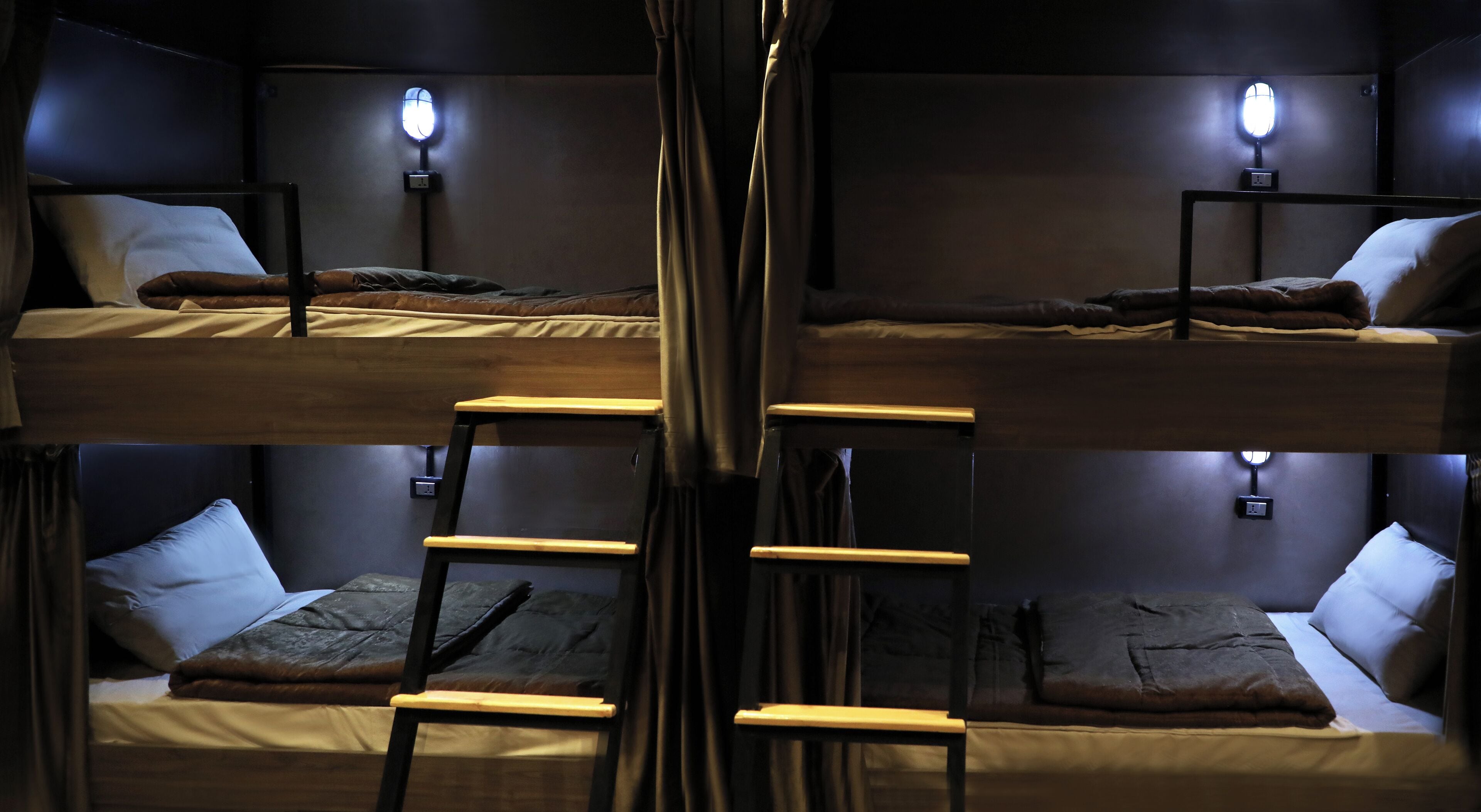 Habitación con literas, dos camas, mesitas de noche y lámparas fijadas a la pared. Una escalera une las camas.