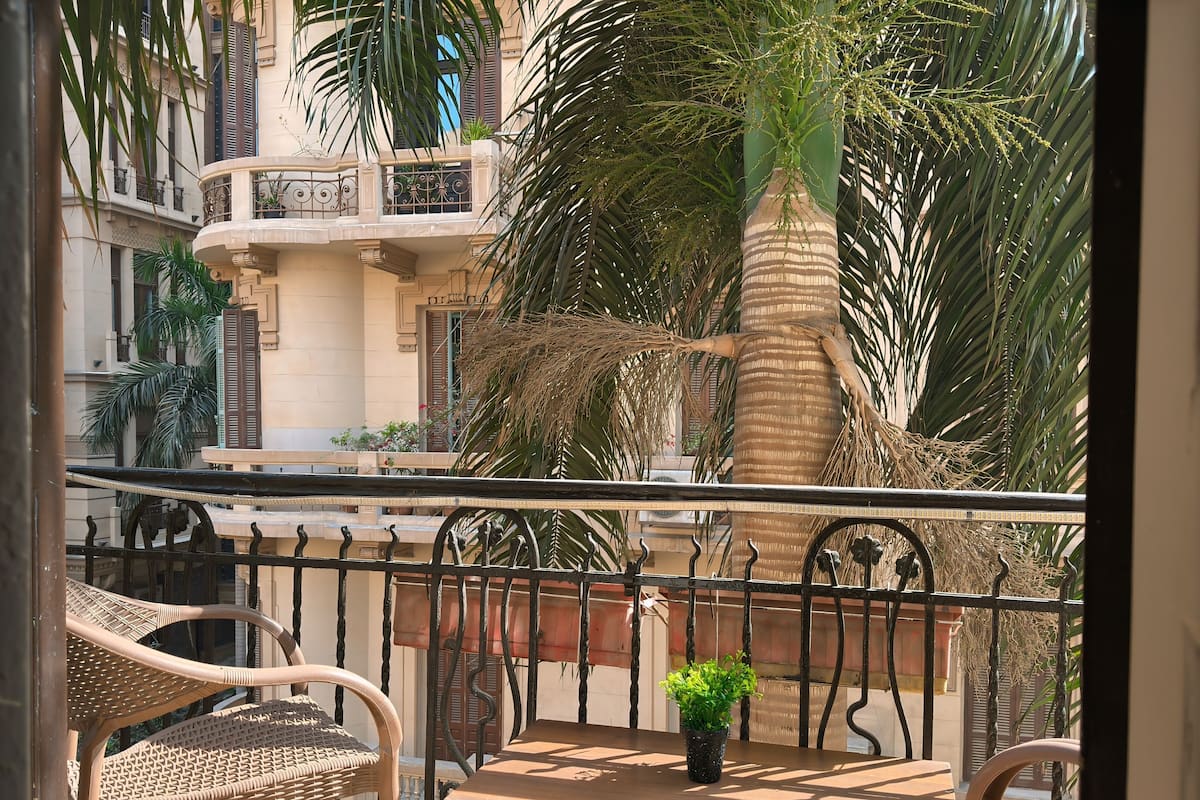 A balcony with wicker chairs, a table, and a potted plant.