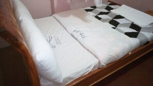 A bed with a white mattress, a checkered pillow, and a white blanket. - Bongo Restaurant & Hotel (Nairobi)