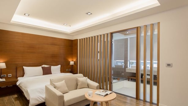A modern hotel room with a large bed, a sofa, a small round table, and a sliding glass door leading to a balcony. - Ai Mei Homestay (Huxi)