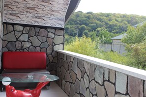 A balcony with a glass table and a red chair, stone wall, and a view of a forested area. - Guba Panoramic Villa (Quba)