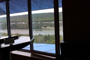 A room with a large window offering a view of a river and distant buildings. - Guba Panoramic Villa (Quba)