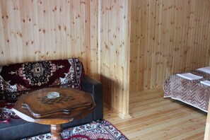 A room with a wooden floor, a sofa with a patterned throw, a small wooden table with a chessboard, and a bed with a patterned bedspread. - Guba Panoramic Villa (Quba)