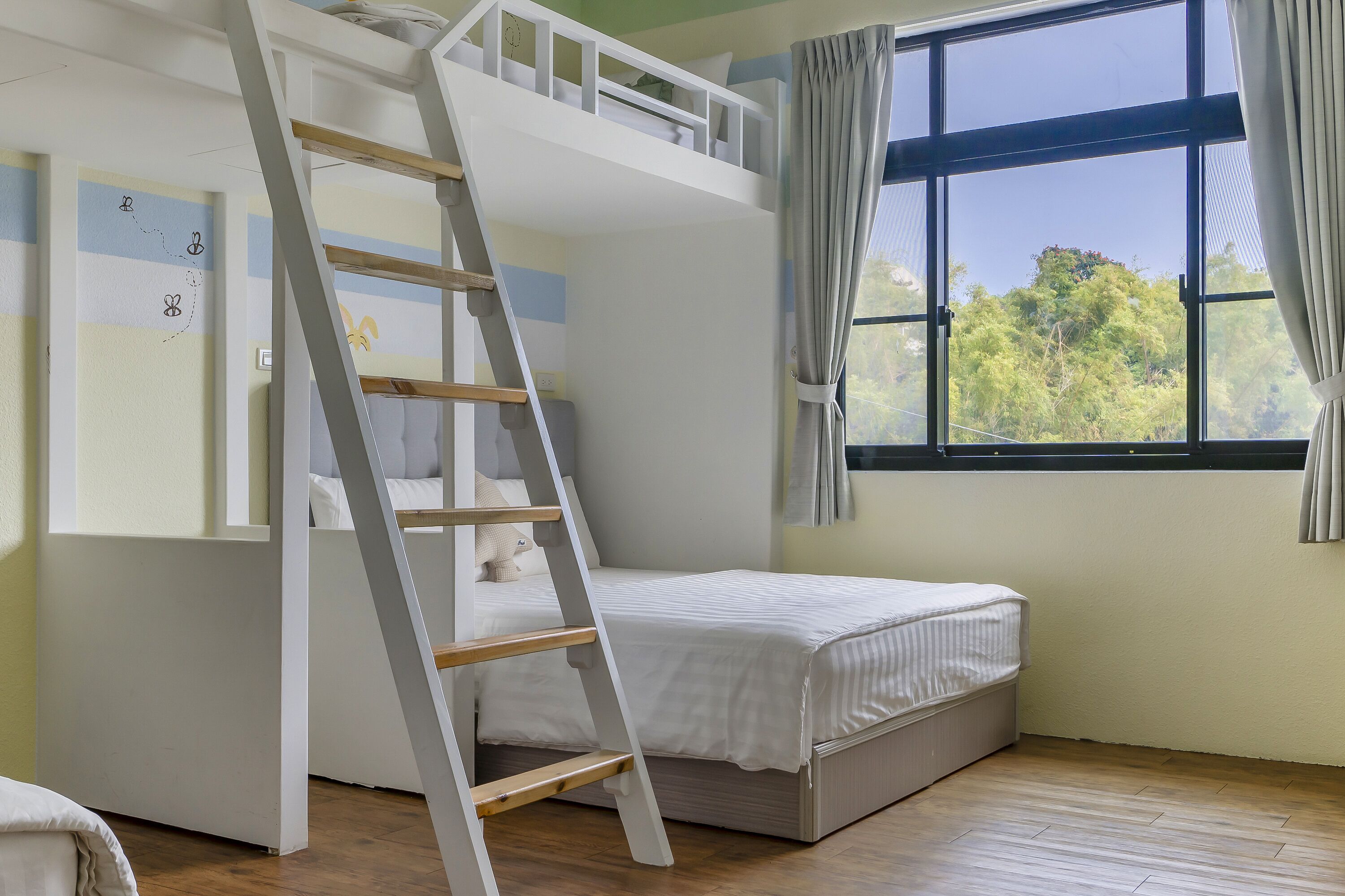 A bunk bed room with a ladder, a window with curtains, and a wall with a butterfly design.