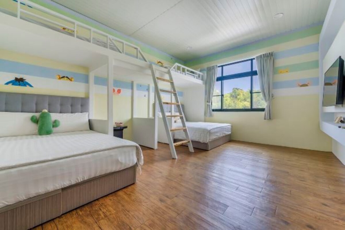 Una habitación con una cama individual superior, una escalera, una ventana con cortinas y una pared con motivos a rayas.
